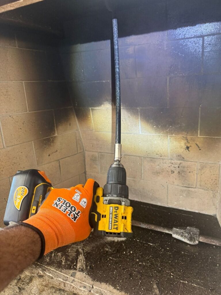 Professional chimney cleaning using a power drill brush attachment by Reliant Chimney Sweeps, ensuring thorough removal of creosote and soot buildup.