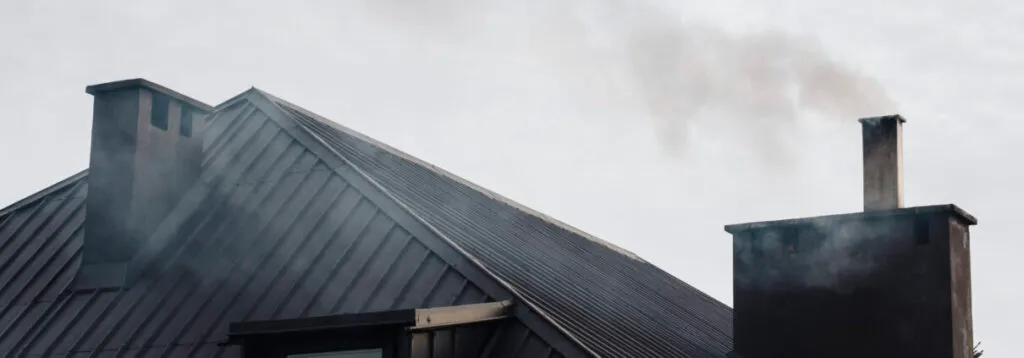 Two chimneys on a roof emitting smoke into the sky.
