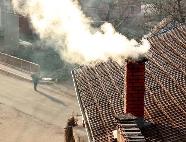 Smoke coming out of a chimney with a person walking on the road below.